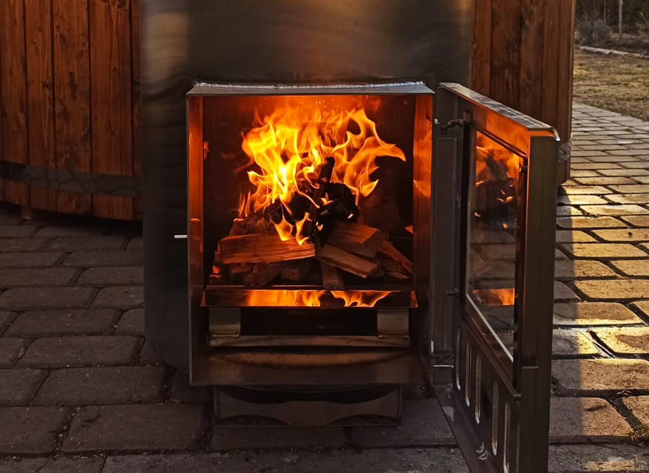 Dunkler Metall-Ofen an einem Feuerbad Hot Tub mit geöffneter Tür. Brennendes Holz ist zu sehen