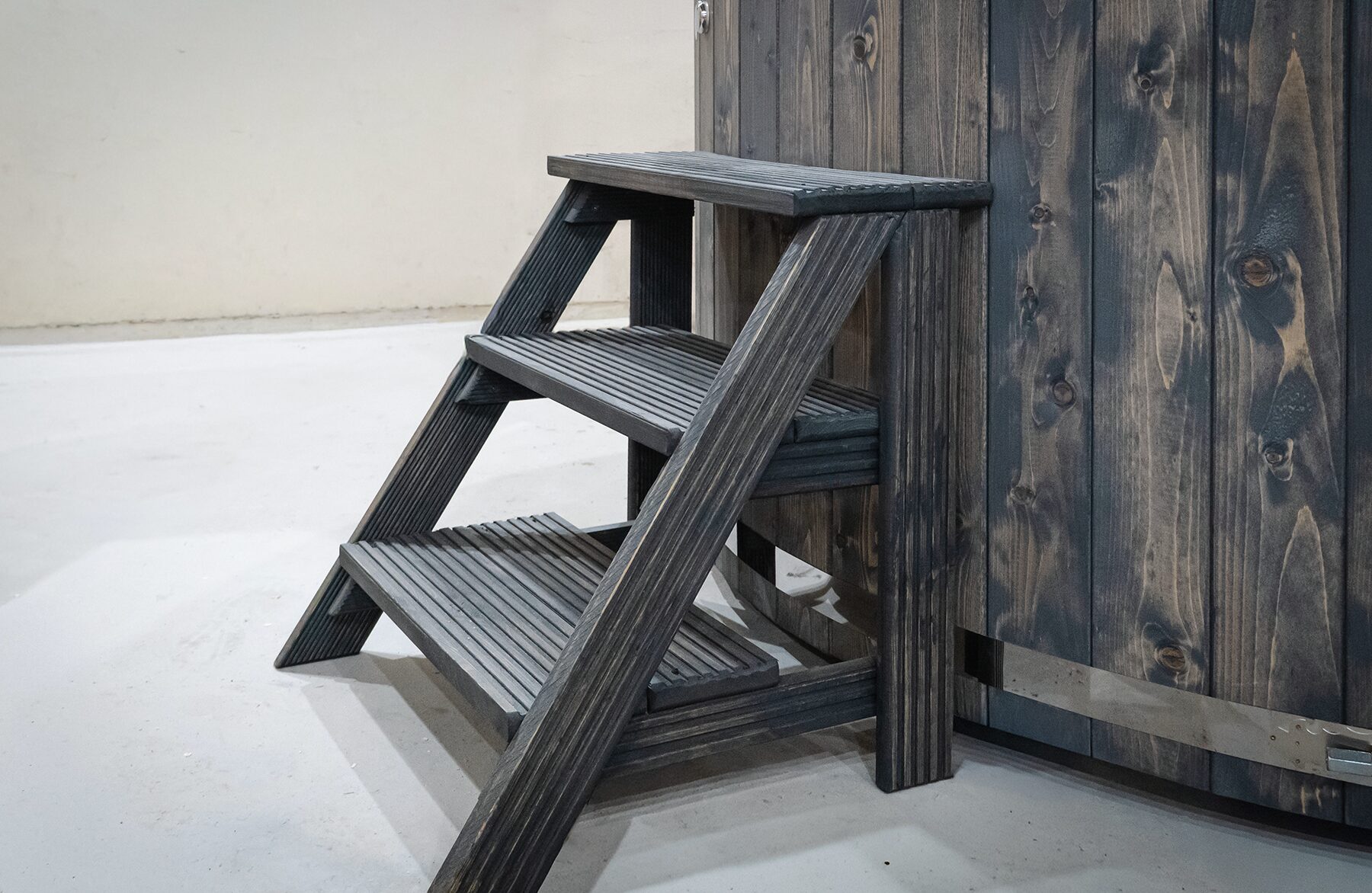 Holz-Einstiegstreppe mit drei Stufen aus dunklem Holz, platziert neben einem Feuerbad Hot Tub LUNA mit Holzverkleidung