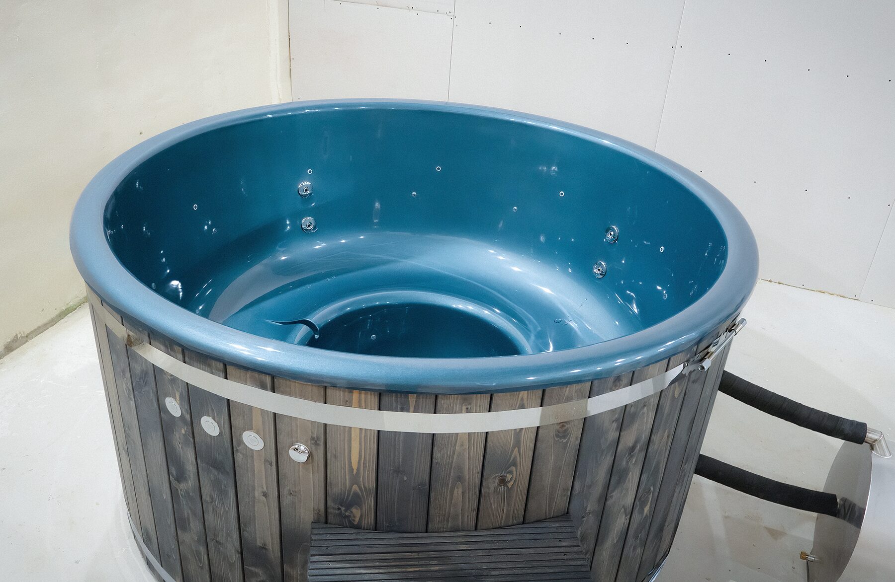 Feuerbad Hot Tub LUNA mit blauer Innenwanne, integrierten Düsen, dunkler Holzverkleidung, und Edelstahlband, ist angeschlossen an einen Metallofen