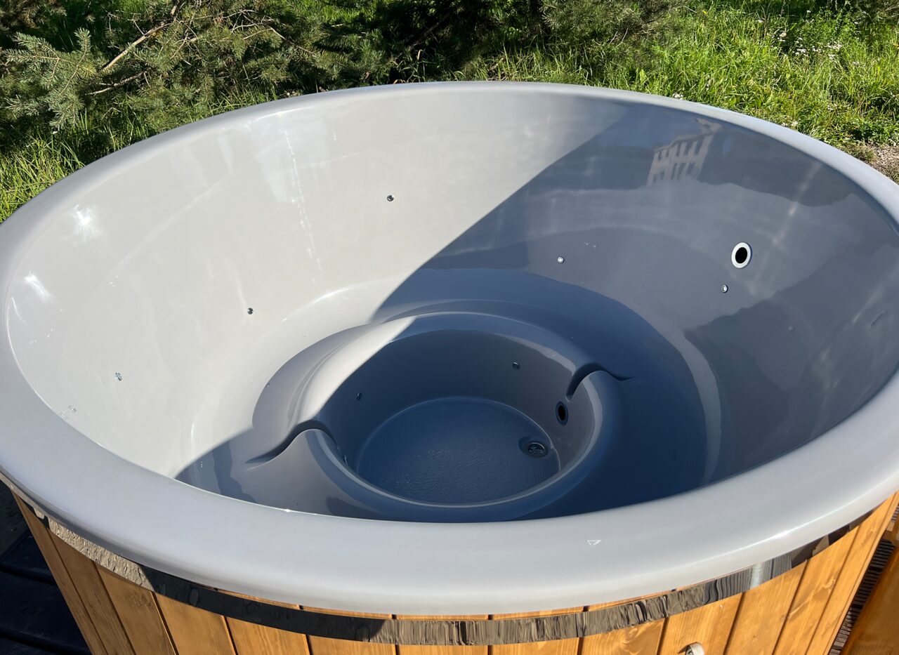Detailansicht der grauen Innenwanne des Feuerbad Hot Tubs LUNA mit ergonomischer Sitzform, integrierten Düsen und Wasserablauf, umgeben von Holzverkleidung im Außenbereich. 