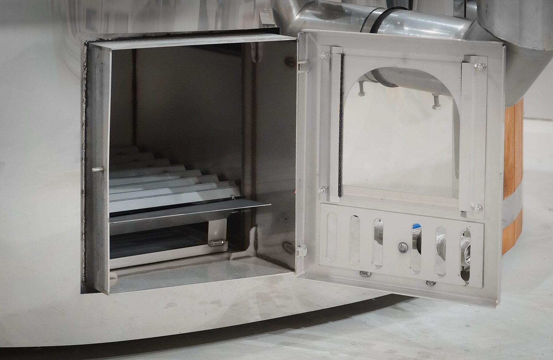 Geöffneter Metallofen eines Feuerbad Hot Tubs SOPHIA mit sichtbarem Feuerraum, Brennkammer und Luftzufuhr, inklusive Rohranschluss im Inneren