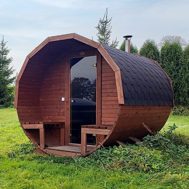 Feuerbad Fass-Sauna JUNO auf einer Wiese mit Bäumen und blauem Himmel im Hintergrund