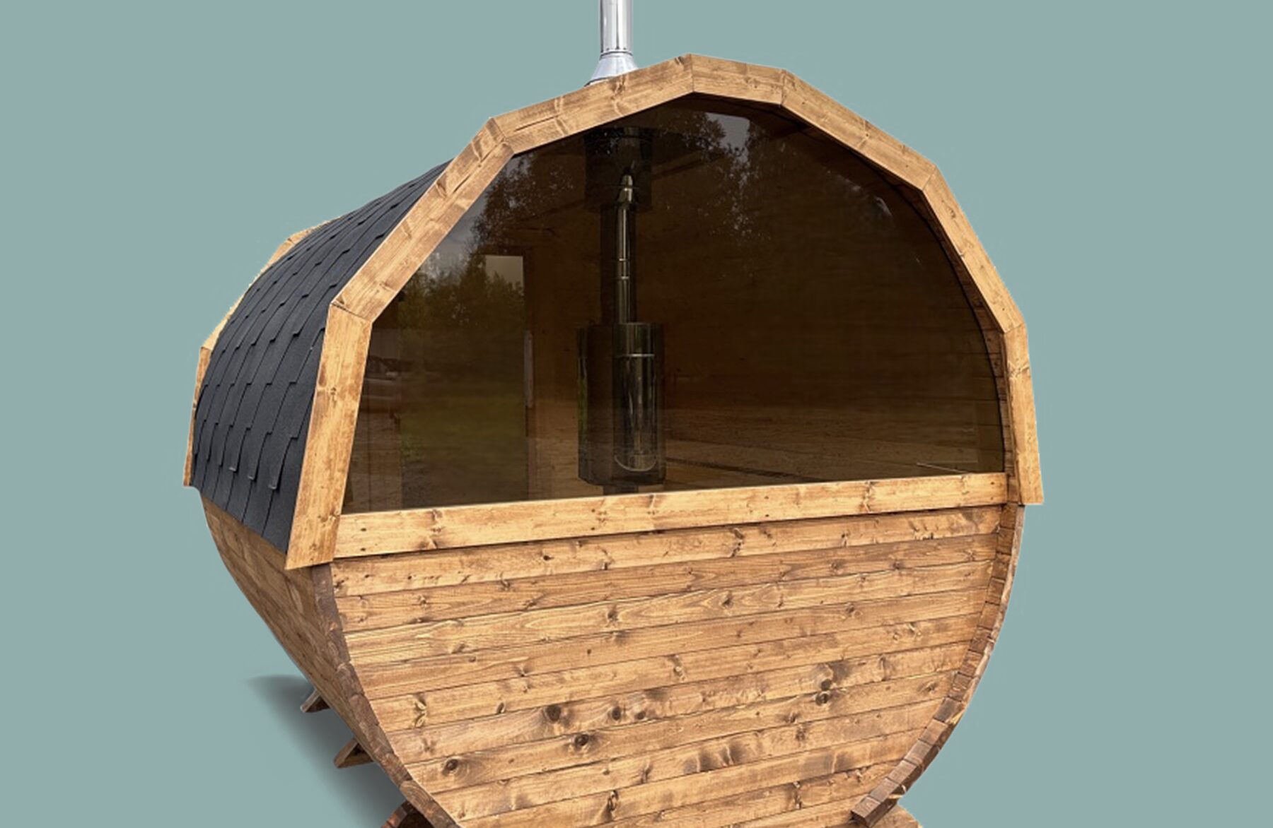 Frontansicht der Feuerbad Fass-Sauna JUNO in runder Fassform mit natürlicher Holzverkleidung, großem Panoramafenster aus Glas, schwarzem Schindeldach und Schornstein, vor neutralem Hintergrund