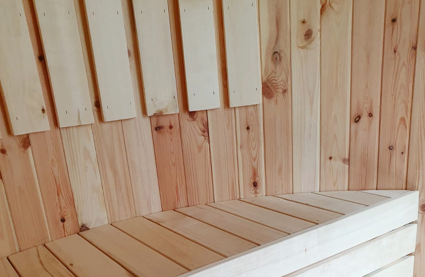 Detailansicht der Sitzbank der Feuerbad Sauna VESTA mit glatter, heller Holzoberfläche, sauber verarbeiteten Holzbrettern und natürlicher Maserung an Wand und Bank