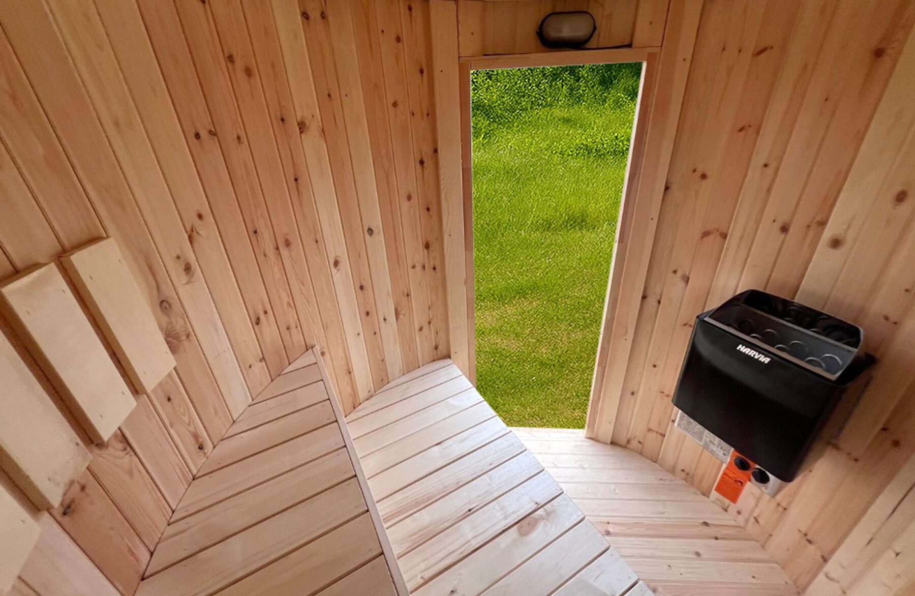 Innenansicht der Feuerbad Sauna VESTA mit heller Holzverkleidung, ergonomisch angeordneten Holzbänken, Holzboden, geöffneter Tür mit Blick ins Grüne und einem schwarzen Saunaofen an der Wand