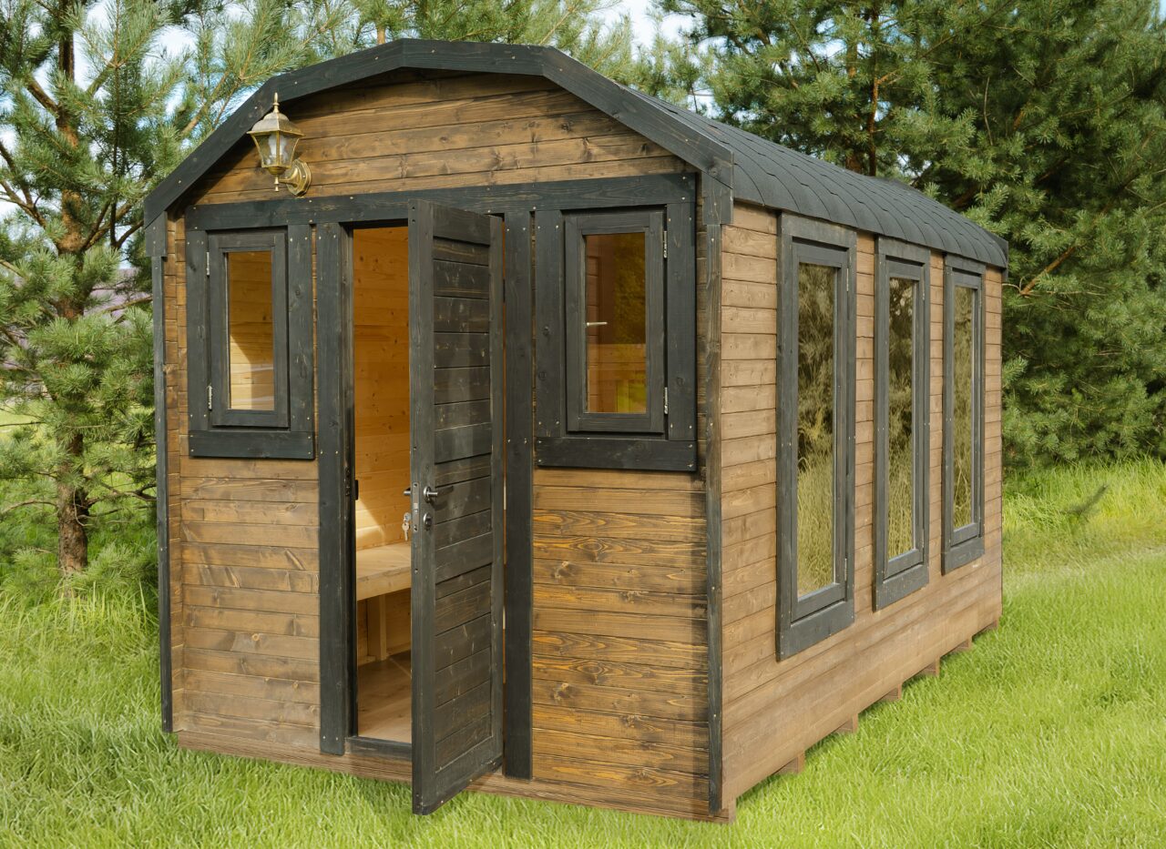 Außenansicht eines Feuerbad Tiny House CERES mit brauner Holzverkleidung und schwarzen Fenster- und Türrahmen. Die Eingangstür steht offen und gibt den Blick auf den hellen Holzinnenraum frei. Das Tiny House steht auf einer grünen Wiese und ist von Bäumen umgeben, was eine naturnahe und ruhige Umgebung vermittelt